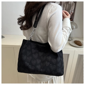 Close-up of black tote bag featuring embossed heart patterns and silver chain strap