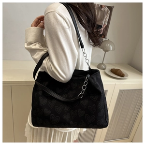 Side view of a black heart-patterned tote bag with silver chain straps worn by a model