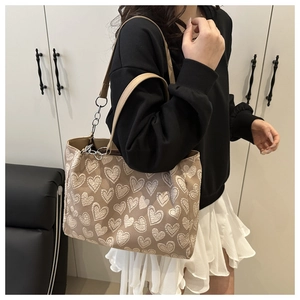 Detail view of heart-patterned tote bag with silver chain and khaki shoulder strap