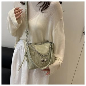Détail du sac bandoulière vert clair avec papillon argenté et texture brillante