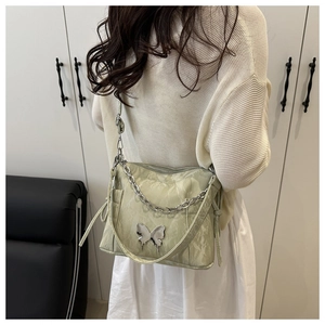 Détail du sac bandoulière vert clair avec papillon argenté et chaîne sur le mannequin