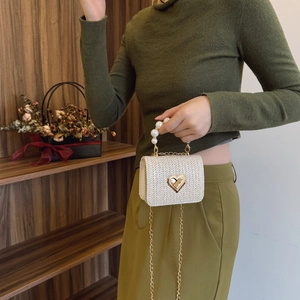 Straw weave mini flap bag with heart lock and white faux pearl handle shown on model