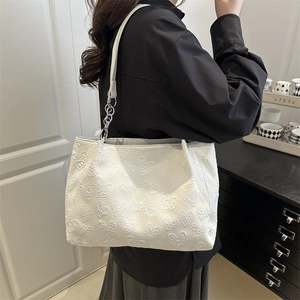 Chic white tote bag with embossed heart pattern and metallic chain strap worn by model