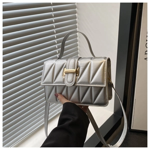 Détail d'un sac bandoulière argenté matelassé avec surpiqûres et boucle dorée