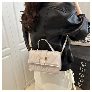 Sac bandoulière beige matelassé avec fermoir doré porté par un mannequin