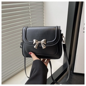 Close-up of black crossbody bag featuring a striking silver metal bow on plain leather