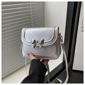 Close-up of silver bow buckle and metallic texture on a small crossbody square bag