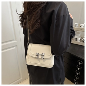 Detail shot of cream leather crossbody bag featuring a decorative silver metal bow clasp
