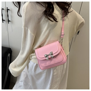 Close-up of pink leather crossbody bag with silver bow accent worn by a model