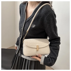 Detail einer cremeweißen Tasche mit Kroko-Prägung, Goldschnalle und Kettenriemen am Modell