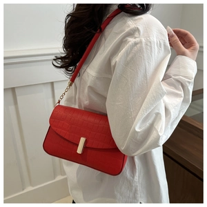 Detail of red croc-embossed shoulder bag featuring a gold buckle and chain accent