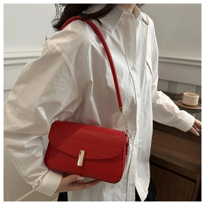 Close-up of red crocodile embossed leather shoulder bag with gold metal buckle detail
