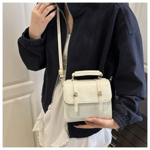 Détail d'un sac bandoulière crème chic avec boucles dorées vintage et une petite forme carrée