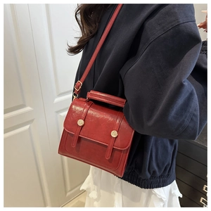 Détail d'un sac à main rouge vintage en cuir avec boucles dorées porté par un mannequin