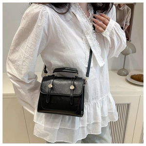 Détail d'un petit sac bandoulière en cuir PU noir avec boucles dorées et poignée supérieure
