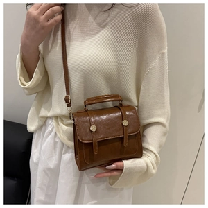 Détail d'un sac bandoulière marron porté avec un pull beige et une jupe blanche plissée