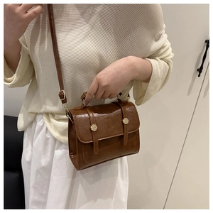 Gros plan d'un sac à bandoulière vintage marron en similicuir avec boucles dorées porté