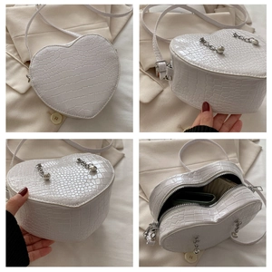 Detail view of heart-shaped crossbody bag with crocodile texture and silver chain