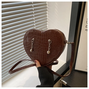 Detail of dark brown heart-shaped bag with faux crocodile skin texture and silver chains