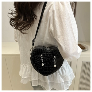 Detail of black crocodile texture heart-shaped crossbody bag with silver chain charms