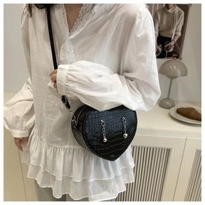 Detail of black heart-shaped crossbody bag with crocodile pattern and silver chain charms