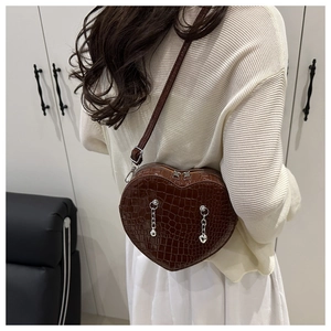 Detail of a dark brown heart-shaped crossbody bag with crocodile pattern and silver chains