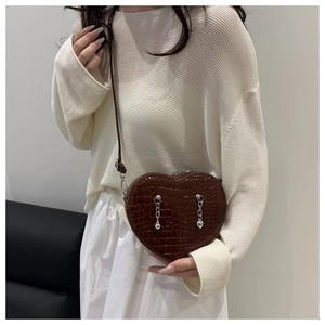 Detail shot of heart-shaped crossbody bag featuring brown crocodile pattern and silver chains