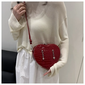 Close-up of a red heart-shaped shoulder bag featuring crocodile texture and silver chains