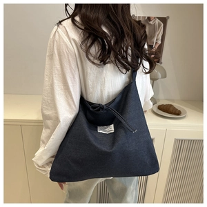 Detail of blue denim tote bag with fashion label and drawstring knot on shoulder