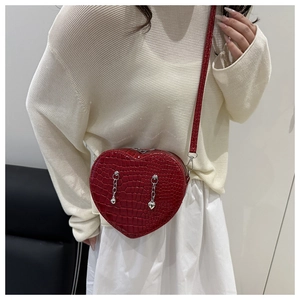 Detail of red heart-shaped crossbody bag with crocodile texture and silver chains