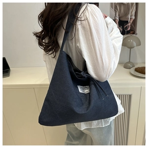 Detail of blue denim tote bag showing drawstring closure and fabric texture on a shoulder bag