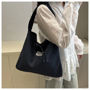 Detail of dark denim tote bag with wide shoulder strap and white woven label on side