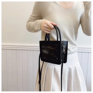 Close-up of black crossbody bag with clear window and adjustable strap on a model