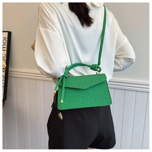 Détail d'un sac bandoulière tressé vert vif avec pointe en métal doré et rabat enveloppe