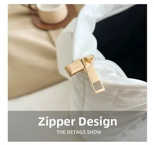 Close-up of golden metal zipper on a white quilted tote bag with shiny finish
