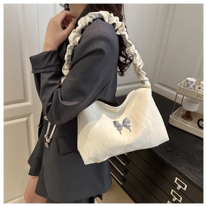 Détail d'un sac à bandoulière plissé blanc crème avec ornement papillon en métal argenté