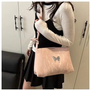 Détail d'un sac à bandoulière rose clair plissé avec emblème papillon argenté et sangle