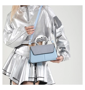 Detail of light blue two-tone handbag with silver arched handle and long shoulder strap
