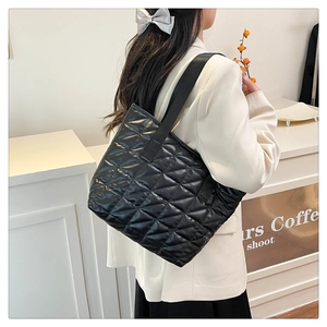 Detail of black quilted tote bag with satin finish shown on model in a minimalist studio