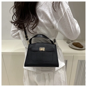Detail of black textured leather handbag with gold twist lock worn by a model