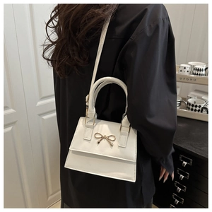 Close-up of a white vintage handbag with a gold bow metal buckle and chain strap