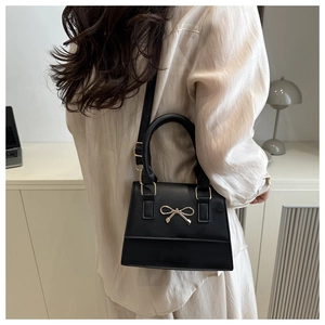 Detail of black PU leather handbag featuring a metal bow buckle and crossbody strap
