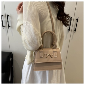 Detail view of a beige crossbody bag with a golden metal bow and elegant leather strap