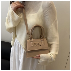 Detail of beige crossbody bag with golden bow hardware and elegant top handle