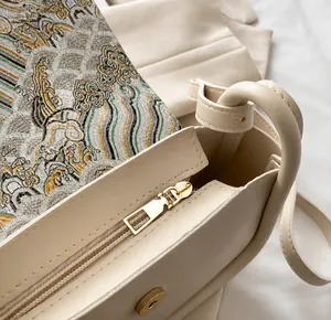 Close-up of smooth golden zipper and embroidery detail on a beige square handbag