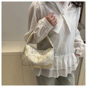 Detail of cream fabric bag with gold butterfly and star embroidery on model shoulder