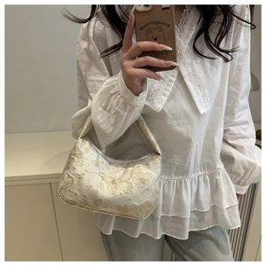 Detailed embroidery of gold butterflies on a cream pillow bag shown in mirror selfie