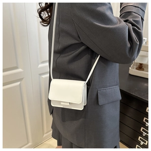 Mini white square crossbody bag with shoulder strap shown on a grey blazer outfit