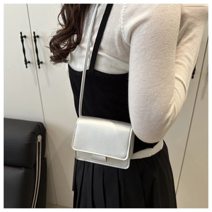 Detailed view of a metallic silver crossbody square bag worn by a model in a modern interior