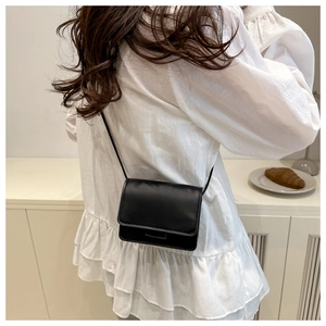 Minimalist black square crossbody bag shown on model in a modern interior setting